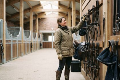 Femme en workwear ajuste des brides dans un box de stabulation