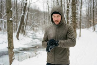 Homme en course d'hiver regardant sa montre sur un sentier enneige