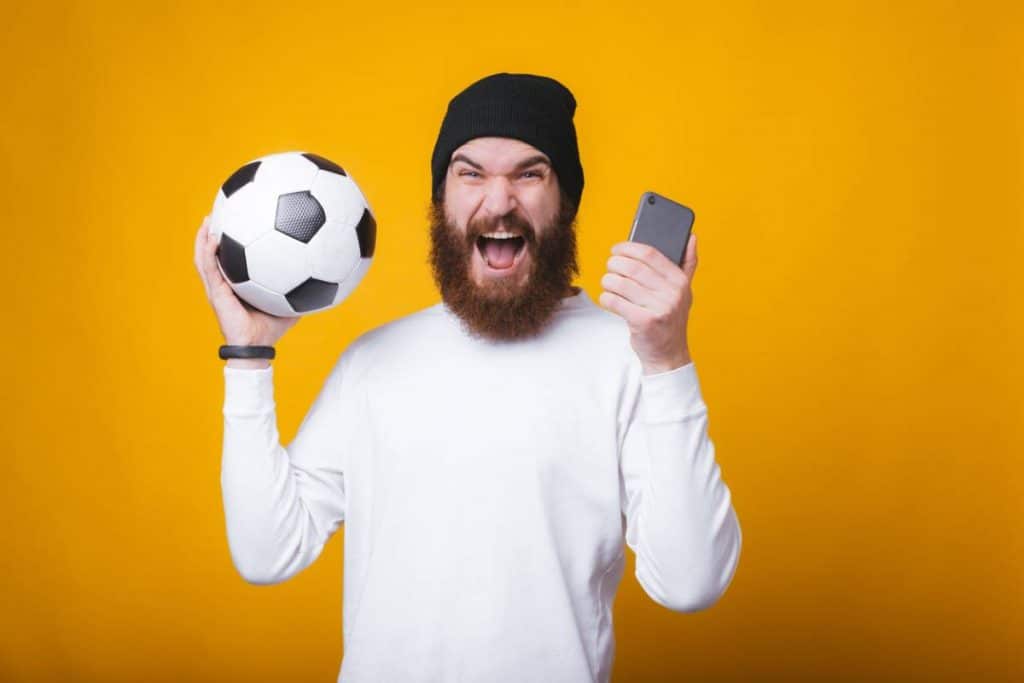 Un homme content avec un ballon de football et un smartphone