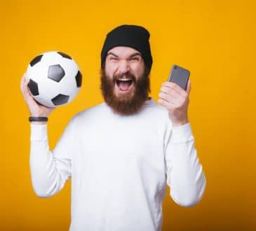 Un homme content avec un ballon de football et un smartphone