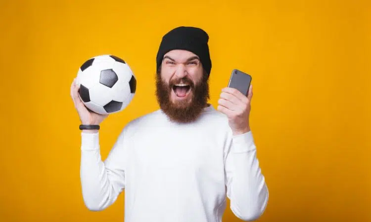Un homme content avec un ballon de football et un smartphone