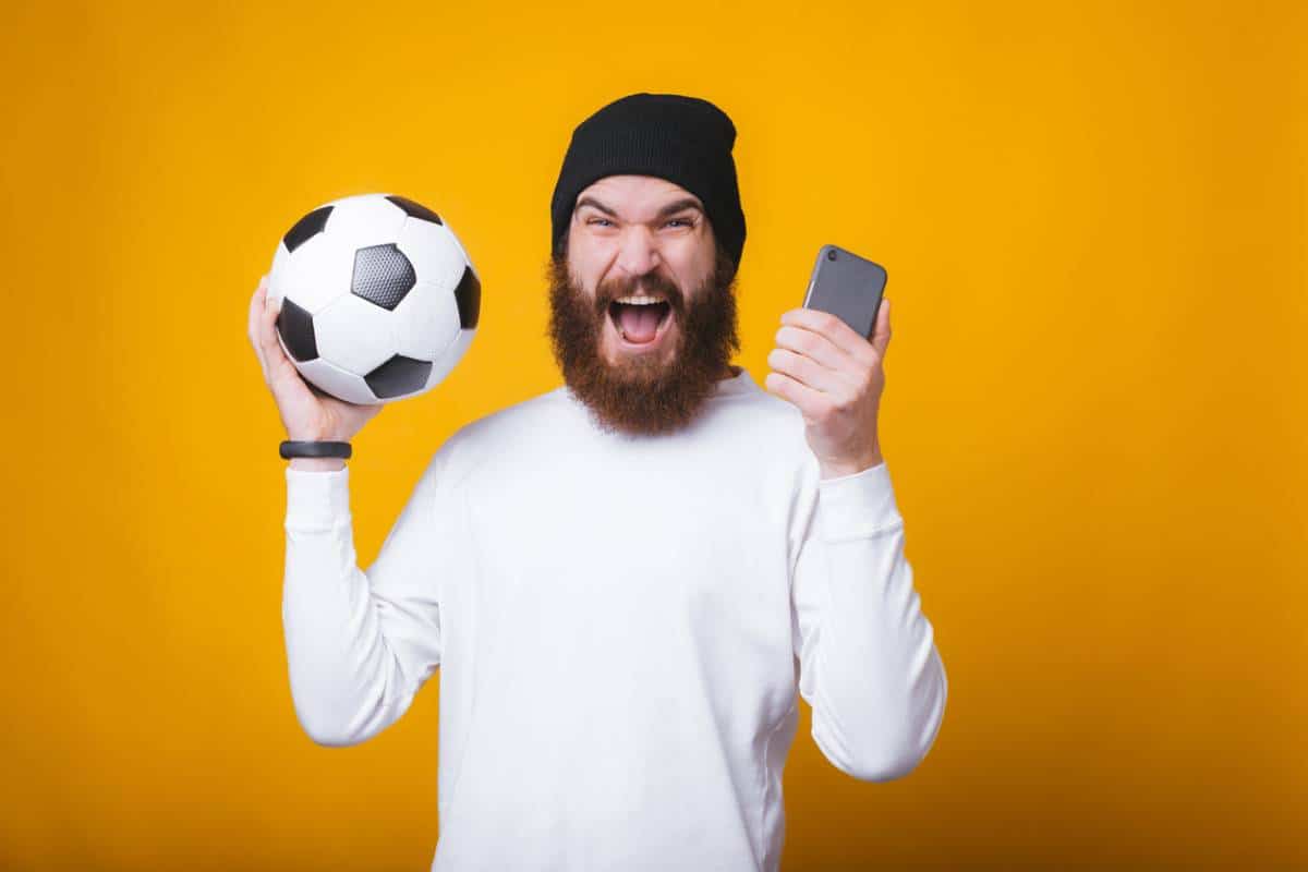 Un homme content avec un ballon de football et un smartphone