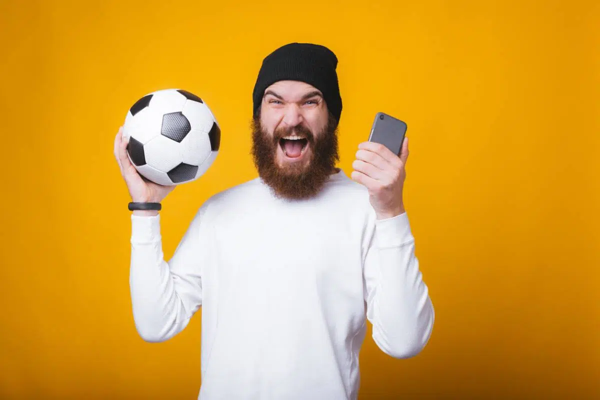 Un homme content avec un ballon de football et un smartphone